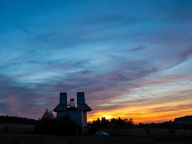 Expo Sternwarte.png Eine Silhouette einer Windmühle vor einem leuchtenden Abendhimmel.