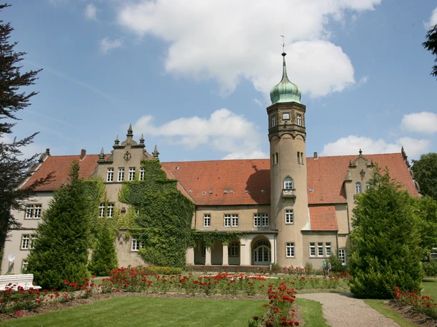 Ein historisches Schloss mit einem imposanten Turm in einer gepflegten Gartenlandschaft.