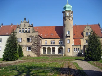 4.Schloß Ulenburg4.JPG Historisches Schloss mit rotem Ziegeldach, Eckturm mit grünem Dach, umgeben von gepflegtem Rasen.