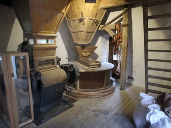 Das Innere einer historischen Windmühle mit hölzernem Mahlwerk und alten Maschinenteilen aus Metall.