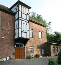 12.Kemenas Mühle.jpg Historische Mühle mit Fachwerkelementen, umgeben von grüner Vegetation und gepflastertem Hof.