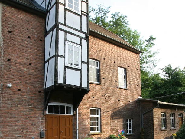 12.Kemenas Mühle.jpg Historische Mühle mit Fachwerkelementen, umgeben von grüner Vegetation und gepflastertem Hof.