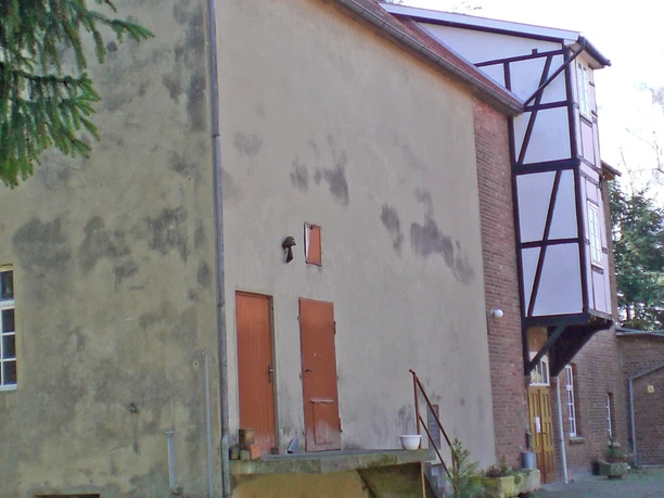 Historische Mühle mit gemauertem Fachwerk und verblasster Putzfassade vor einem klaren Himmel.
