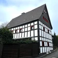 Haus Steeg Fachwerkhaus in Rösrath mit dunklen Balken und weißem Putz, umgeben von Hecken und einem Holzzaun.