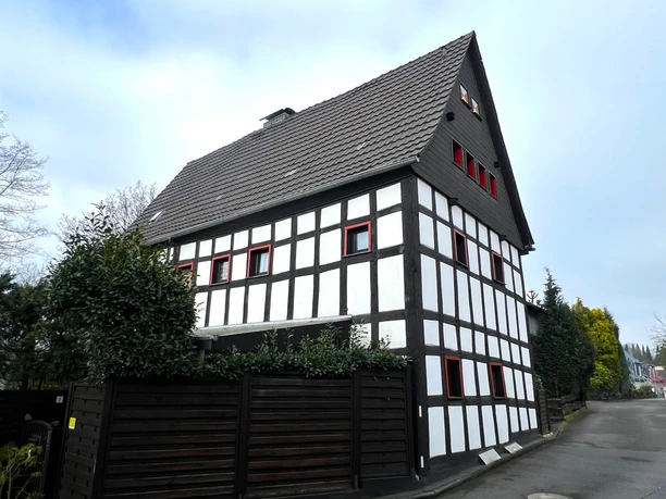 Haus Steeg Fachwerkhaus in Rösrath mit dunklen Balken und weißem Putz, umgeben von Hecken und einem Holzzaun.