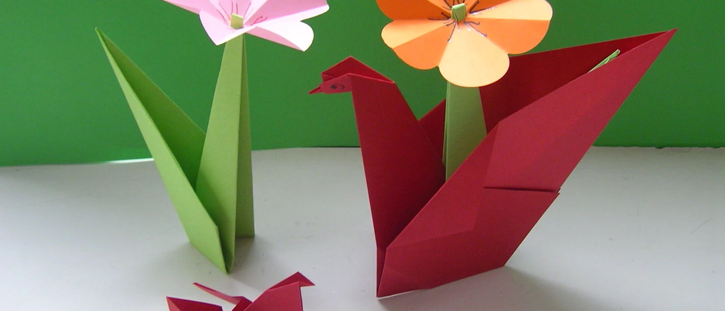 Origami Blumen Origami-Kunst: Zwei Blumen in Grün- und Orangetönen und zwei rote Papierkraniche vor grünem Hintergrund.