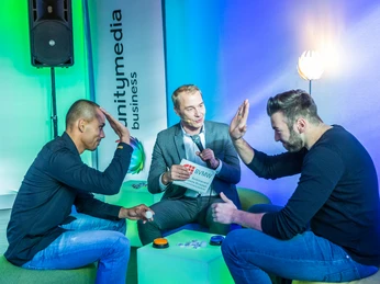 WeQuiz, Messewisser Männer spielen Quiz, Moderator hält Karten, bunte Leuchttische, moderne Umgebung.Men play quiz, moderator holds cards, colorful light tables, modern surroundings.