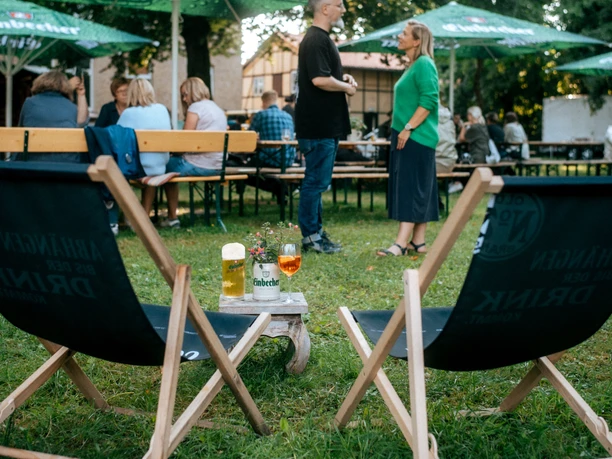 Biergarten in Einbeck Wiese mit Stühlen, Getränken und Menschen.