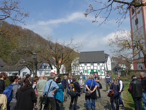 Odenthal Eine Gruppe von Menschen steht auf einem gepflasterten Platz, umgeben von Fachwerkhäusern und Bäumen.