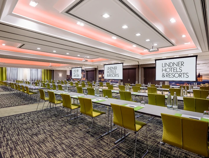 LINDNER Hotel City Plaza; Köln; Cologne; CGNCIT; Tagung; Mühlheim Kalk Porz; 02 Ein großer, hell beleuchteter Tagungsraum mit gelben Stühlen, Tischen und Projektionsleinwänden.A large, brightly lit conference room with yellow chairs, tables and projection screens.