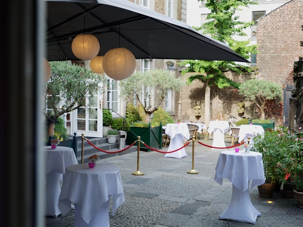 _MG_0013_Bagdu-fuer-Wolkenburg-300dpi_2.jpg Cozy courtyard garden with lanterns, round bar tables and plants under large parasols.