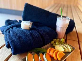 Verwöhn-Paket_Seesauna_b.jpg Wellness-Ambiente mit frischem Obst, Getränk, schwarzen Handtüchern und Creme auf Holztisch.