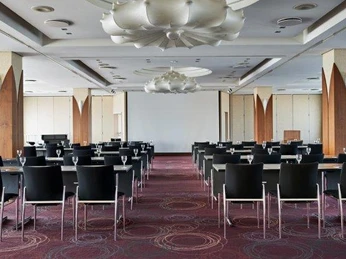 Belvedere Moderner Konferenzraum mit Reihen von schwarzen Stühlen, Tischen und großer Leinwand im Hintergrund.</p>Modern conference room with rows of black chairs, tables and a large screen in the background.</p> <p