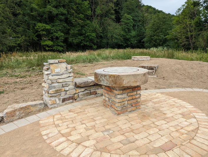 Steinerner Aussichtspunkt mit gepflasterter Fläche und Panorama-Guide, umgeben von Natur.