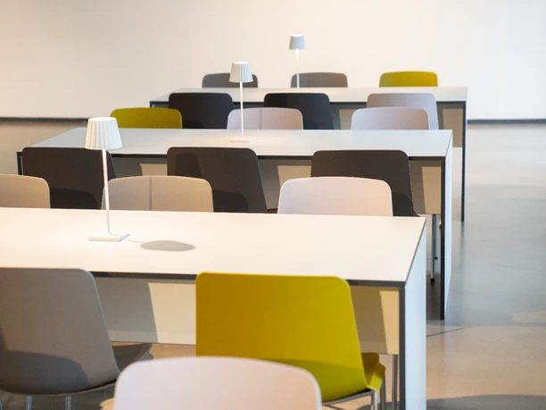 Mietmöbel Tische mit bunten Stühlen und Tischlampen in modernem, minimalistischem Design in einem hellen Raum.