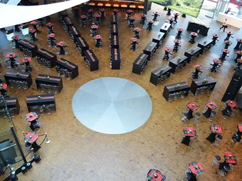 miro-110-schwarz3.jpg Runder Saal mit Holzboden, schwarzem Mobiliar und rot-grün karierten Tischdecken aus der Vogelperspektive.Round hall with wooden floor, black furniture and red and green checkered tablecloths from a bird's eye view.