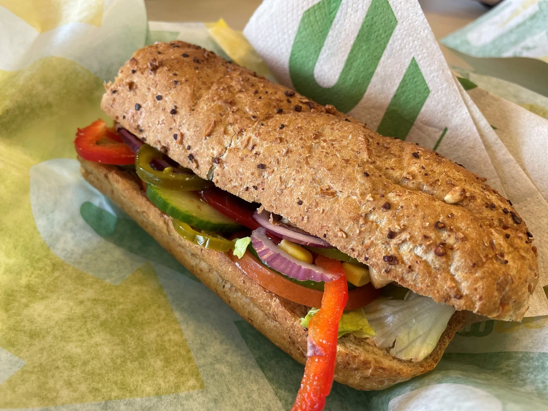 Ein Vollkorn-Sandwich gefüllt mit frischen Paprikastreifen, Salat, Tomaten, roten Zwiebeln und Gurken.