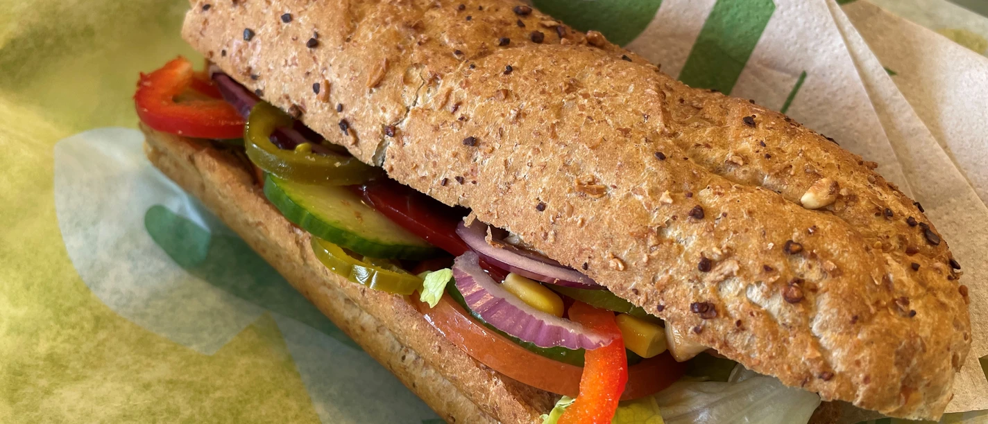 Ein Vollkorn-Sandwich gefüllt mit frischen Paprikastreifen, Salat, Tomaten, roten Zwiebeln und Gurken.