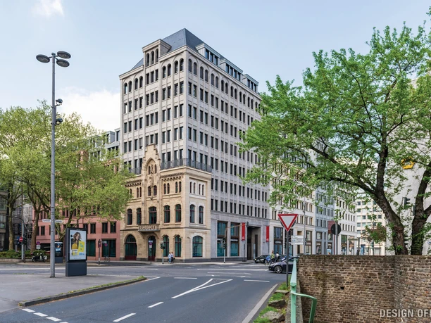 Historic corner building in an urban setting with trees in the foreground and a clear sky.</p> <p