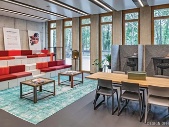Lounge Moderner Arbeitsraum mit farbigen Sitzstufen, Holztischen und Fensterblick ins Grüne.</p>Modern workspace with colorful seating steps, wooden tables and window views of the greenery</p>.