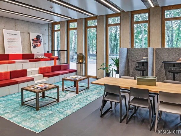 Lounge Moderner Arbeitsraum mit farbigen Sitzstufen, Holztischen und Fensterblick ins Grüne.</p>
