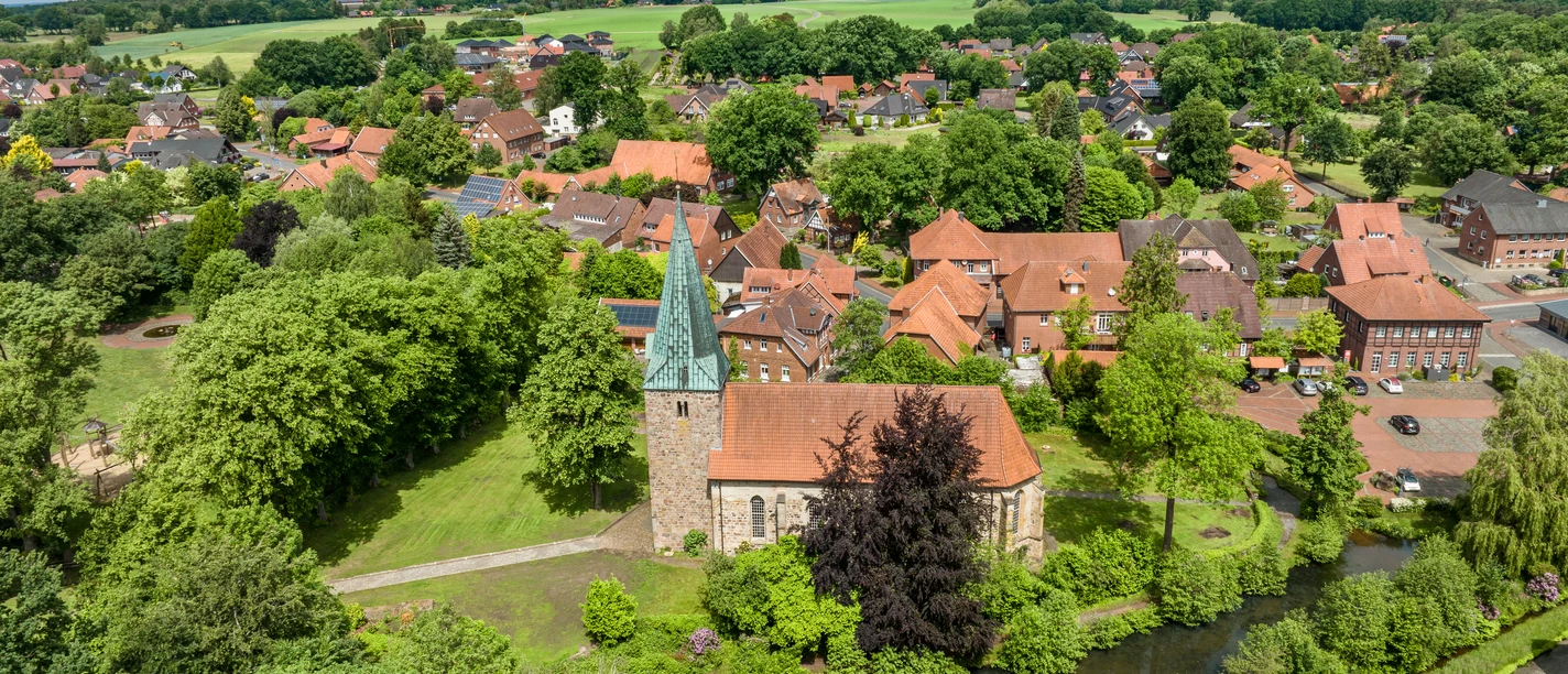 bippen-ortsbild-auteursrecht-tol-foto-max-wiesenbach.jpg Luchtfoto van een stad in Nedersaksen met een kerk, omringd door bomen en velden.