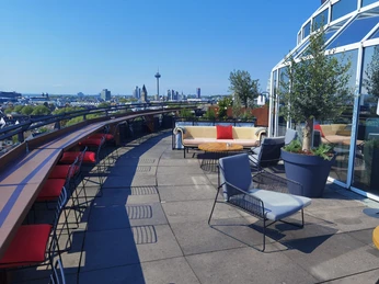 Bar Botanik Außenbereich.jpg Rooftop-Terrasse mit bunten Sitzmöbeln und Blick auf Kölns Stadtpanorama bei klarem Himmel.</p>Rooftop terrace with colorful seating and a view of Cologne's city panorama on a clear day</p>.