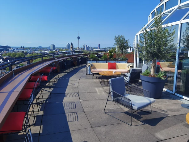 Bar Botanik Außenbereich.jpg Rooftop-Terrasse mit bunten Sitzmöbeln und Blick auf Kölns Stadtpanorama bei klarem Himmel.</p>