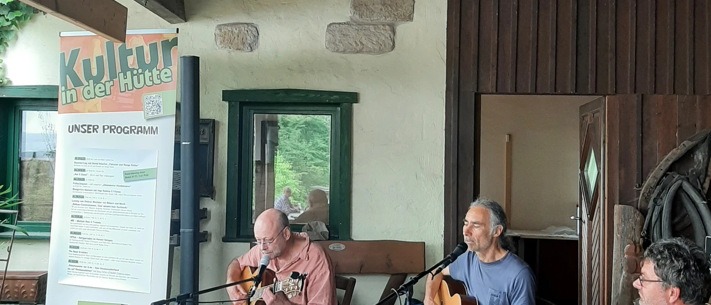 Ingo Halama und Freunde Ingo Halama und Freunde musizieren mit Gitarren unter einem hölzernen Vorbau vor einem Kulturschild.