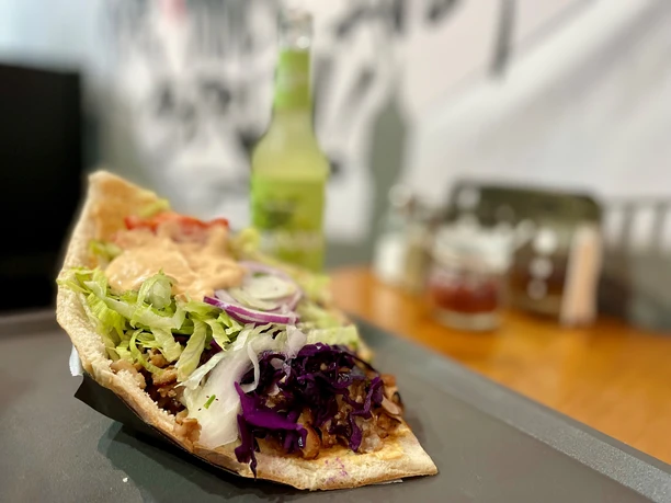 Döner-Kebab mit frischem Salat und roten Zwiebeln auf einem Teller, im Hintergrund eine Limonade.