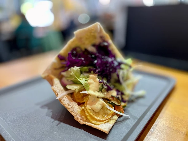 Veggie-Döner mit gegrilltem Gemüse, Rotkohl und Salat, serviert auf einem schwarzen Tablett.