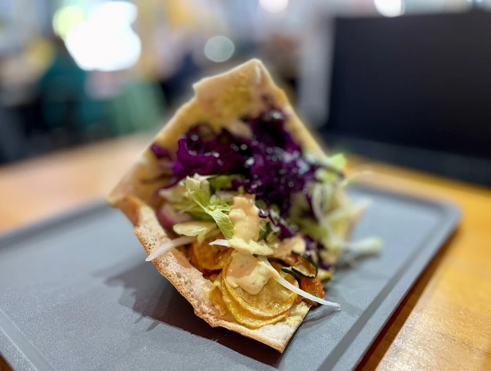 Veggie-Döner mit gegrilltem Gemüse, Rotkohl und Salat, serviert auf einem schwarzen Tablett.