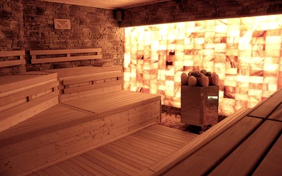 Sauna in der Birkensauna.jpg Eine Holzsauna mit Wänden aus beleuchteten Salzziegeln schafft eine entspannende und warme Atmosphäre.