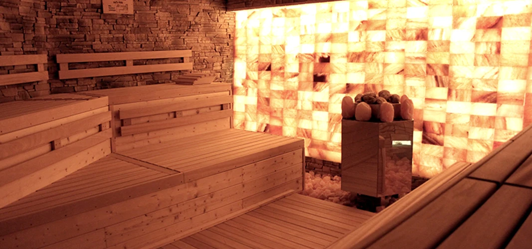 Sauna in der Birkensauna.jpg Eine Holzsauna mit Wänden aus beleuchteten Salzziegeln schafft eine entspannende und warme Atmosphäre.