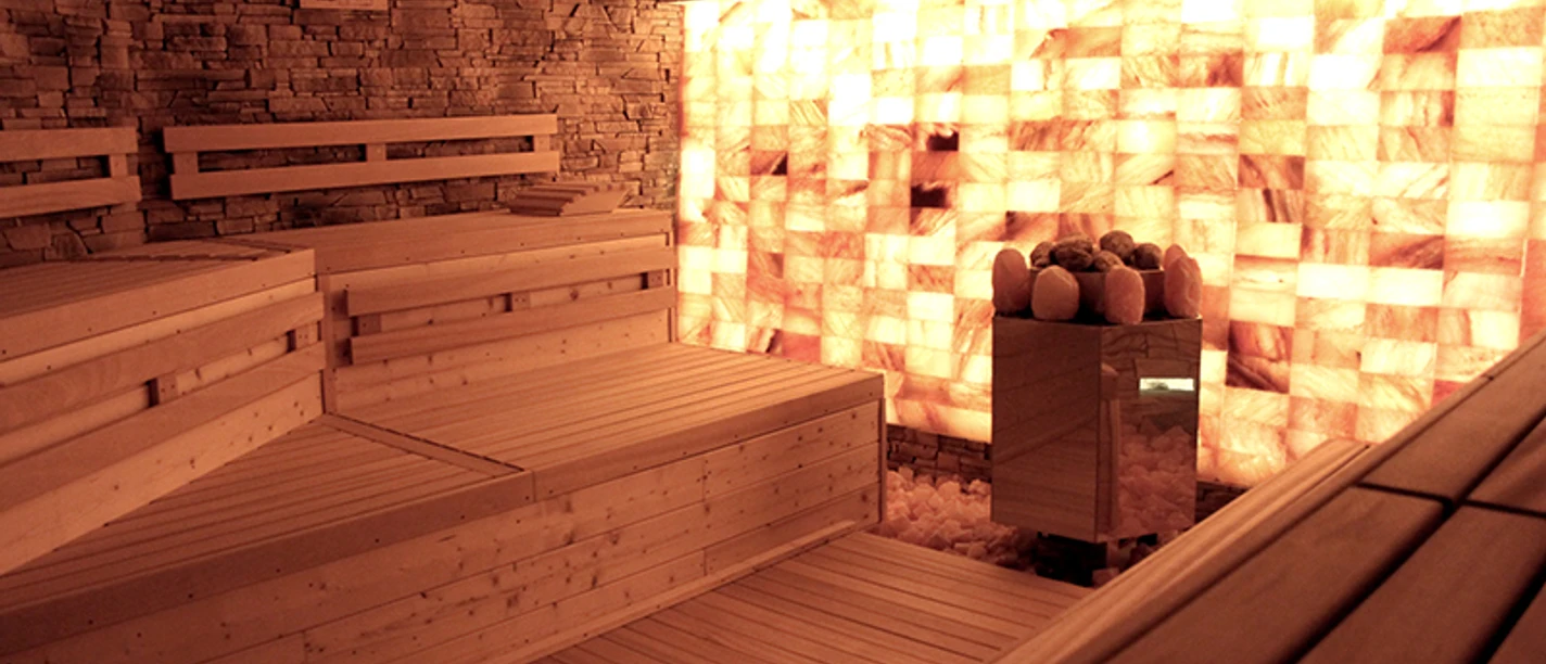 Sauna in der Birkensauna.jpg Eine Holzsauna mit Wänden aus beleuchteten Salzziegeln schafft eine entspannende und warme Atmosphäre.