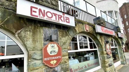 Fassade eines Wein- und Feinkostgeschäfts mit dem Namen Enotria Vino und einem Ristorante in Steinoptik.