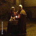 Zwei Personen in historischer Kleidung stehen nachts mit einer Laterne auf gepflasterter Straße.