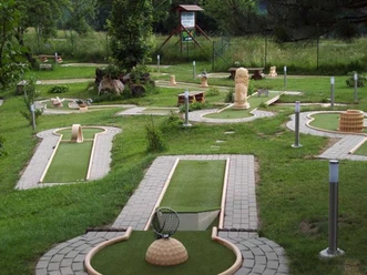Minigolfbaan met verschillende banen en hindernissen, omgeven door groene weiden en bomen; rustige, uitnodigende sfeer.