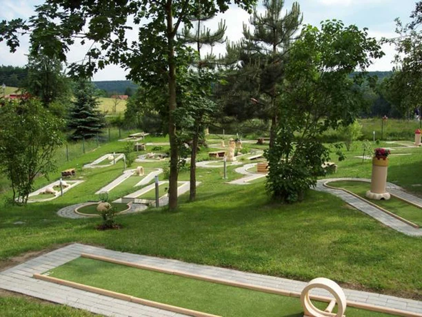 Een minigolfbaan met verschillende holes, omgeven door groene bomen en grasvelden, onder een licht bewolkte hemel.