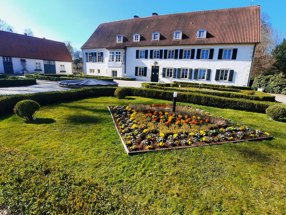 Haus des Gastes FrühjahrTouristik Preußisch Oldendorf.jpg Ein weißes Gebäude mit rotem Ziegeldach und blauen Fensterläden umgeben von gepflegten Gärten.