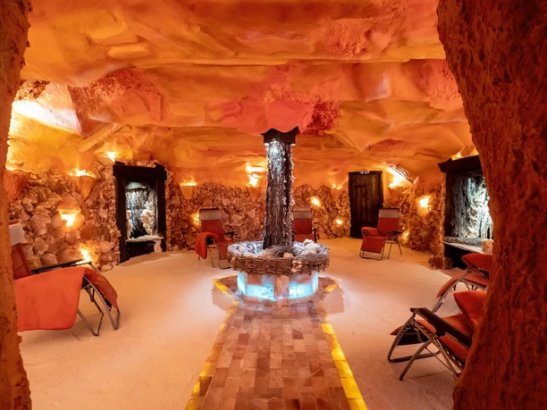 Warm beleuchtete Salzgrotte mit Liegestühlen, Felswänden und zentralem Brunnen