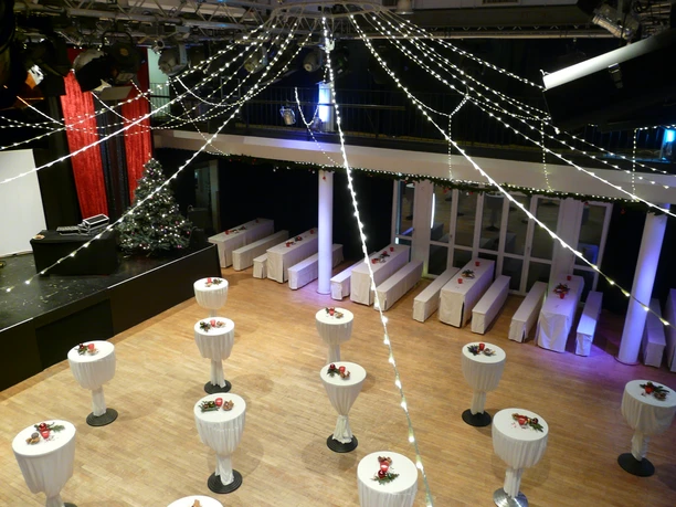 Großer Saal im BHK Rundtische mit weißen Tischdecken in festlich beleuchtetem Bankettsaal, Weihnachtsschmuck auf jedem Tisch.