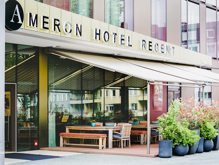 Eingang_Terrasse.jpg Ansicht des Eingangsbereichs vom Ameron Hotel Regent mit Auffahrt und bunten Pflanzen.