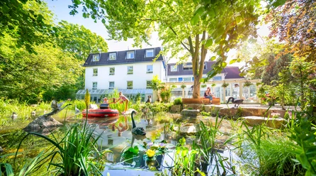 Gartenhotel Fettehenne in Erkrath Gartenhotel Fettehenne in Erkrath mit Teich, grüner Umgebung und moderner weißer Fassade.