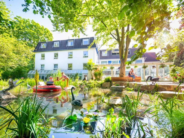 Gartenhotel Fettehenne in Erkrath Gartenhotel Fettehenne in Erkrath mit Teich, grüner Umgebung und moderner weißer Fassade.