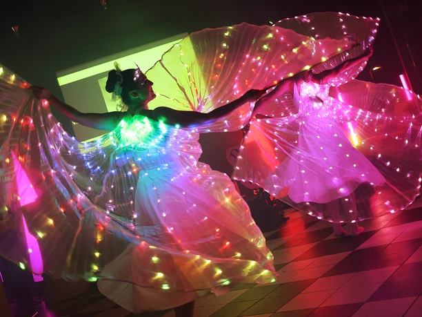 Dancers Lichteffekt-Tänzerinnen mit leuchtenden Flügeln in schimmernden Kostümen auf einer Bühne.