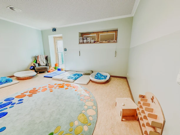 IMG_2025.jpg Heller Schlafraum im Kindergarten mit runden Matratzen und buntem Teppich.