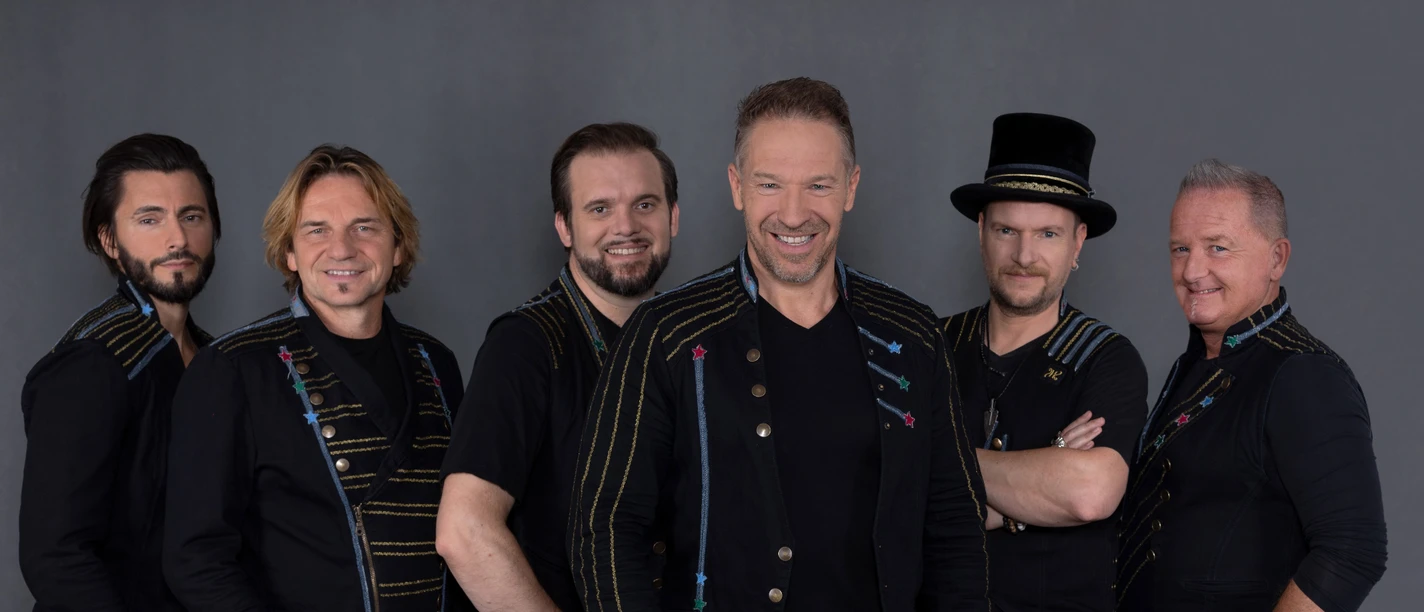 Höhner Six smiling men in black clothing and festive designs pose in front of a gray background.</p> <p