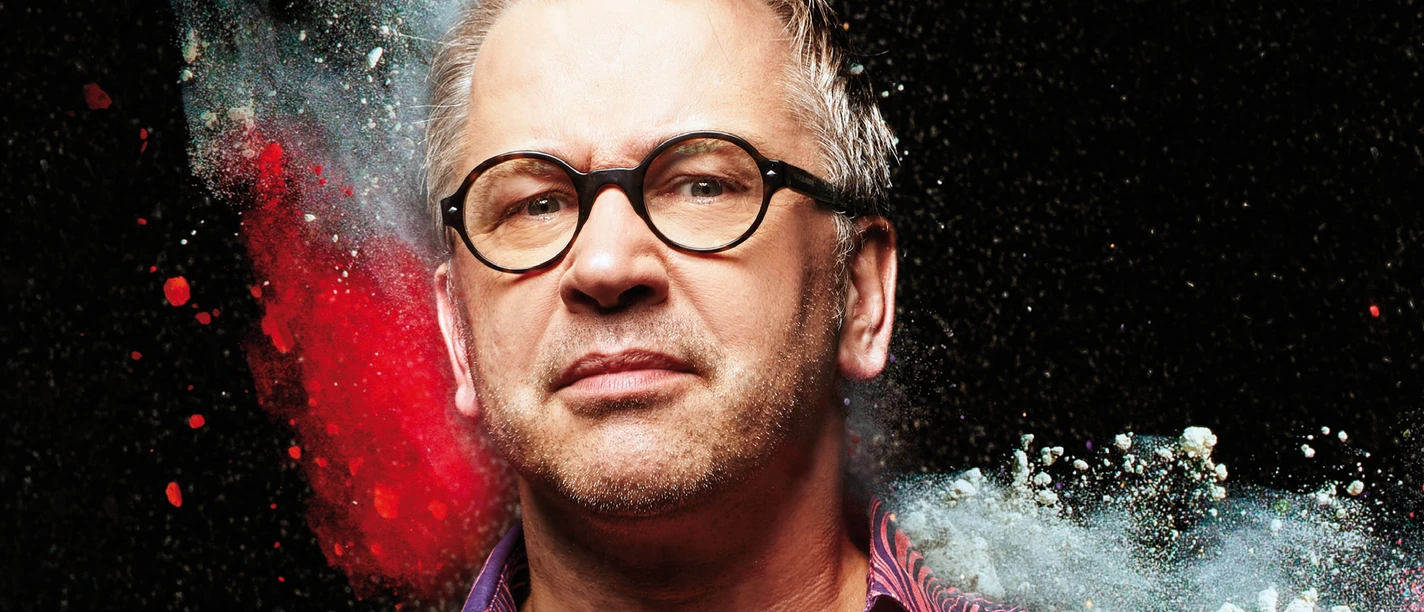 Robert Griess Portrait of a man with glasses in front of a black background, surrounded by colored powder.
