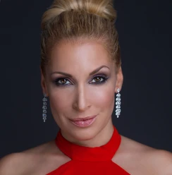 Tatiana Perez Porträt einer eleganten Frau mit blonden Haaren und rotem Kleid vor dunklem Hintergrund.</p>